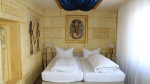 Hotellihuone, jossa on kaksi sänkyä, suuri seinämaalaus, jossa on kuvattuna egyptiläinen esine, ja sininen kattokangas.