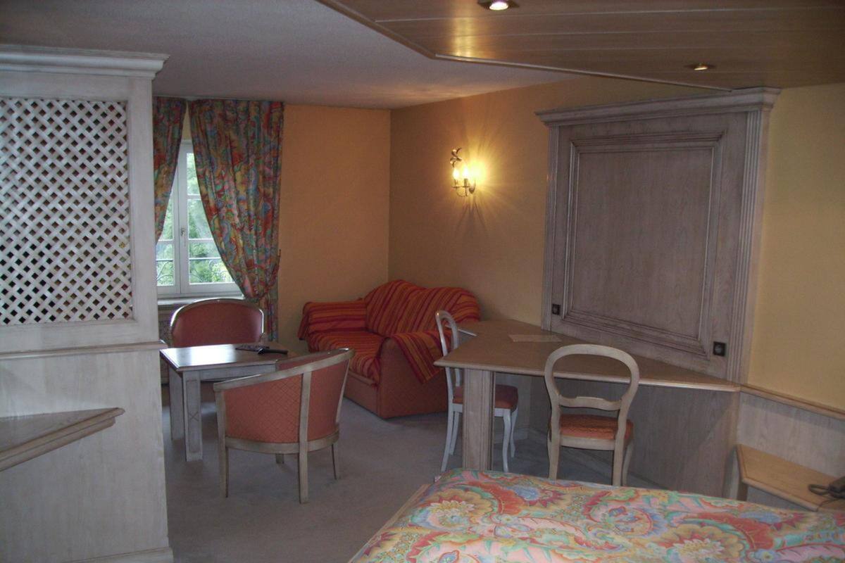 Una habitación con cama, una mesa, dos sillas, un sofá y un ventanal con cortinas.