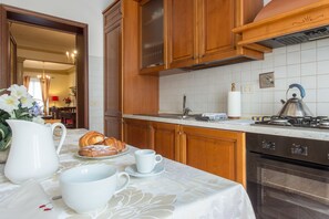 Cozinha com armários de madeira, bancada de mármore, fogão, forno e área de jantar com mesa posta para o café da manhã.
