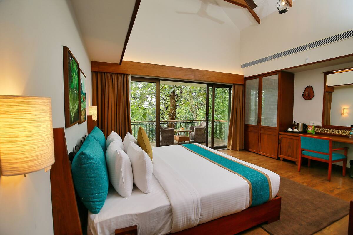 Une chambre d’hôtel avec un grand lit, un bureau et un balcon donnant sur un espace verdoyant.