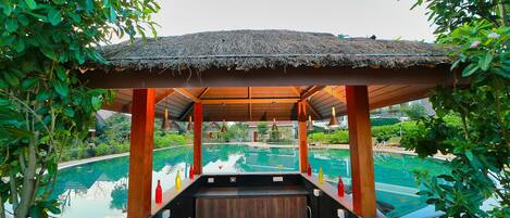 A covered hot tub area with a pool in the background.