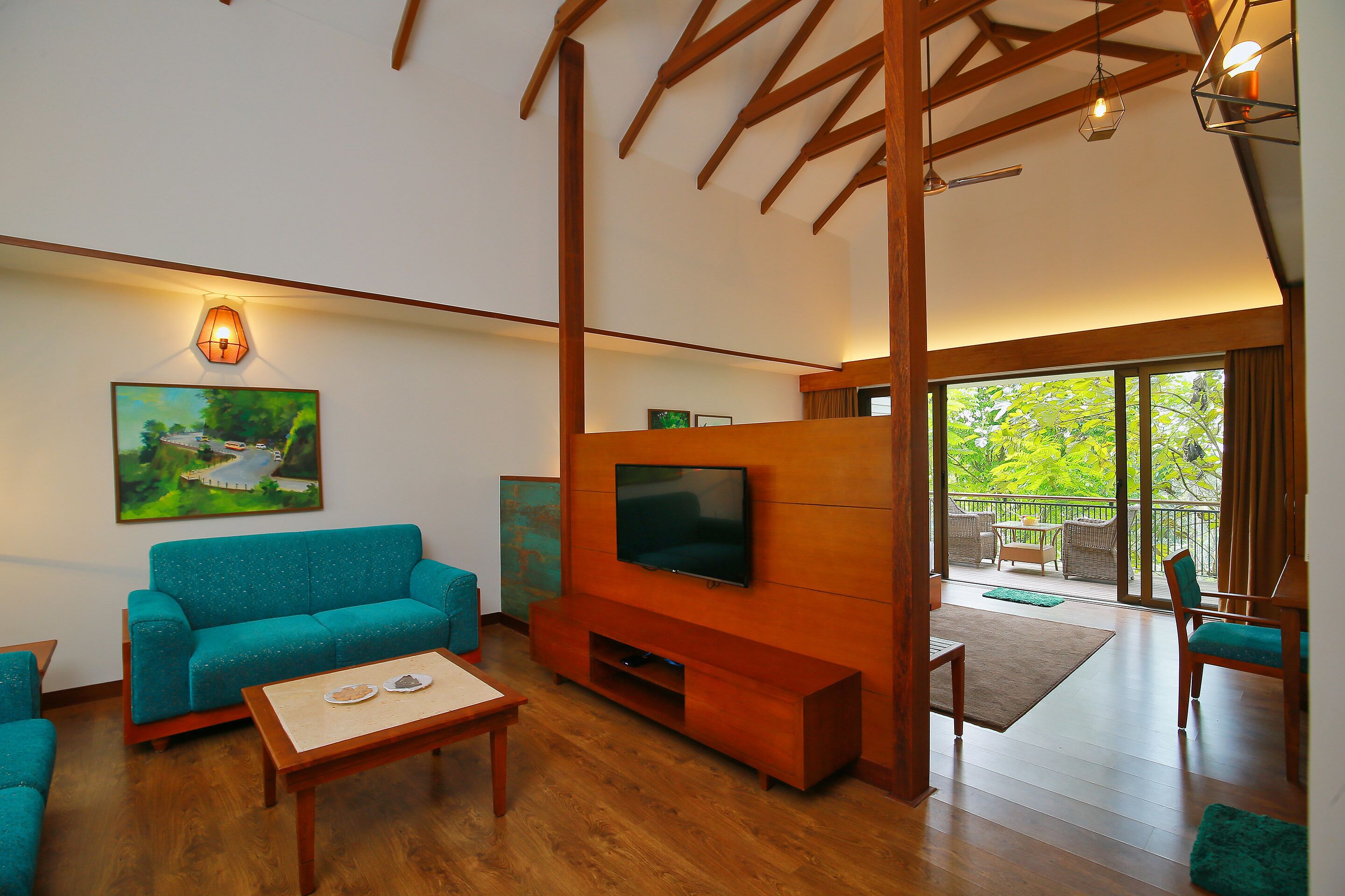 A spacious living room with a large flat-screen TV, wooden beams, a teal sofa, and a view of the outdoors.