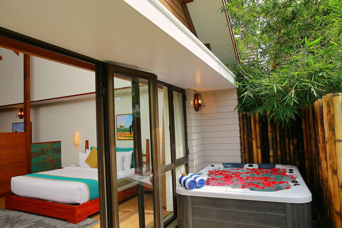 Une chambre d’hôtel moderne dotée d’un grand lit, d’un jacuzzi et offrant une vue sur un jardin de bambous.