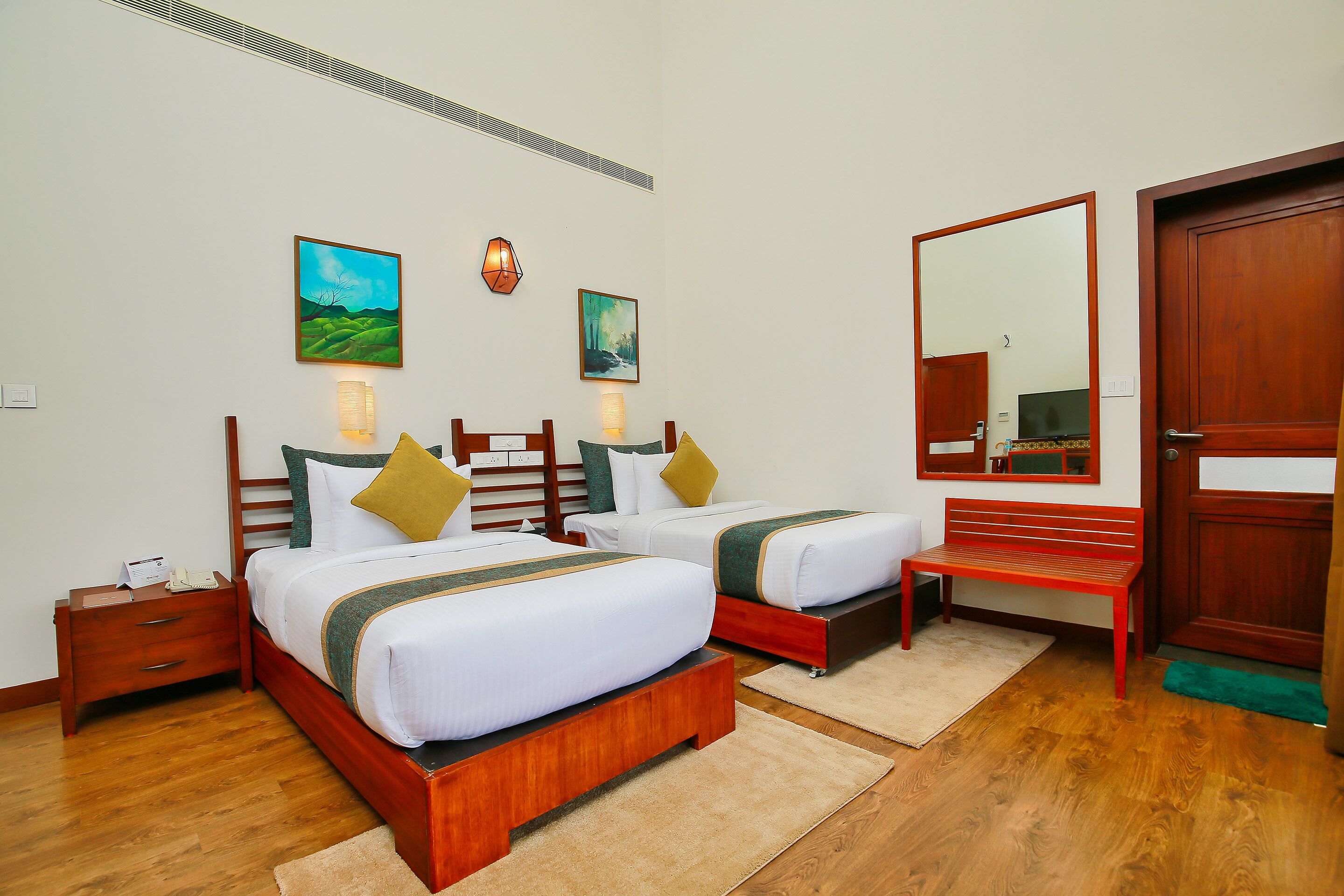 A hotel room with two beds, wooden headboards, a bench, and artwork on the walls.
