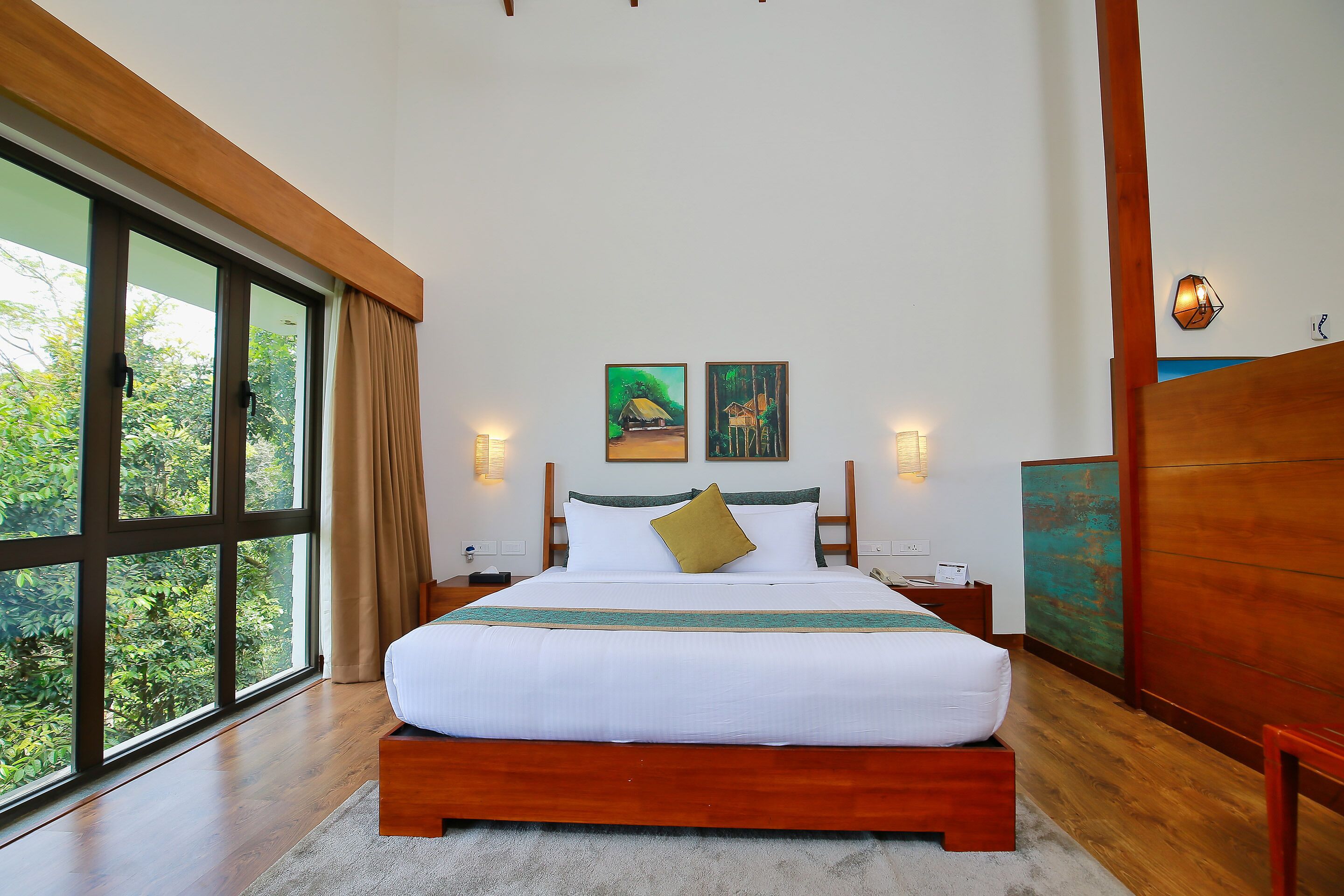 A bedroom with a large window, wooden bed frame, and two paintings on the wall.