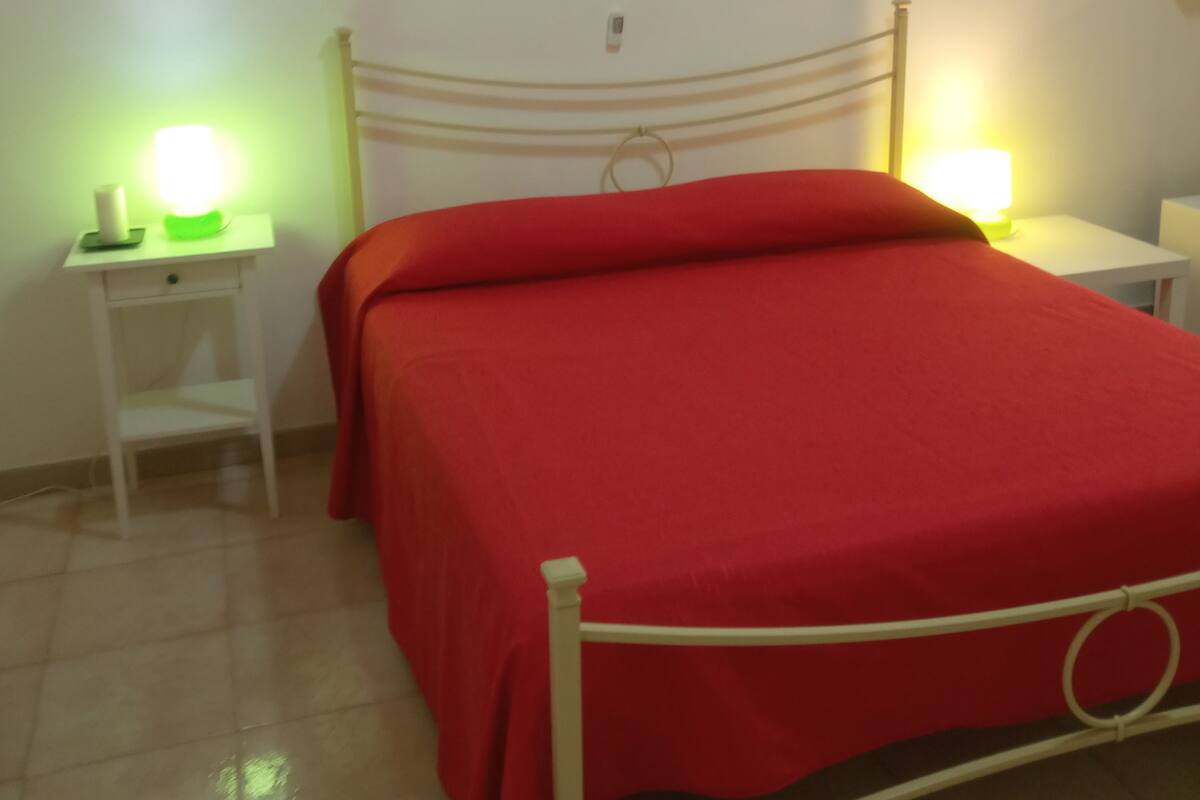 A room with a bed, a nightstand, a lamp, and a painting on the wall.