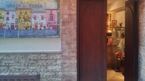 Un muro de piedra con un mural de azulejos que representa edificios coloridos, una puerta de madera y un expositor de vidrio con artículos.