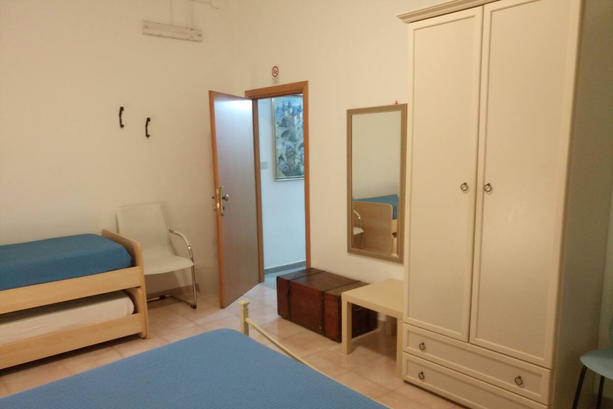 A bedroom with a bed, a chair, a wardrobe, and a mirror.