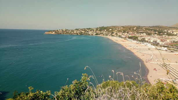 Un pueblo costero con una playa, mar azul cristalino y edificios a lo largo de la orilla.