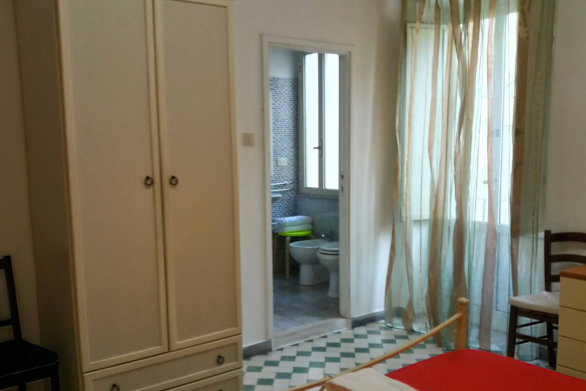 A bedroom with a bed, a wardrobe, a chair, and a view of a bathroom.