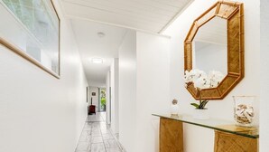 A hallway with a tiled floor, a glass-top console table with a mirror, and a red suitcase in the distance.
