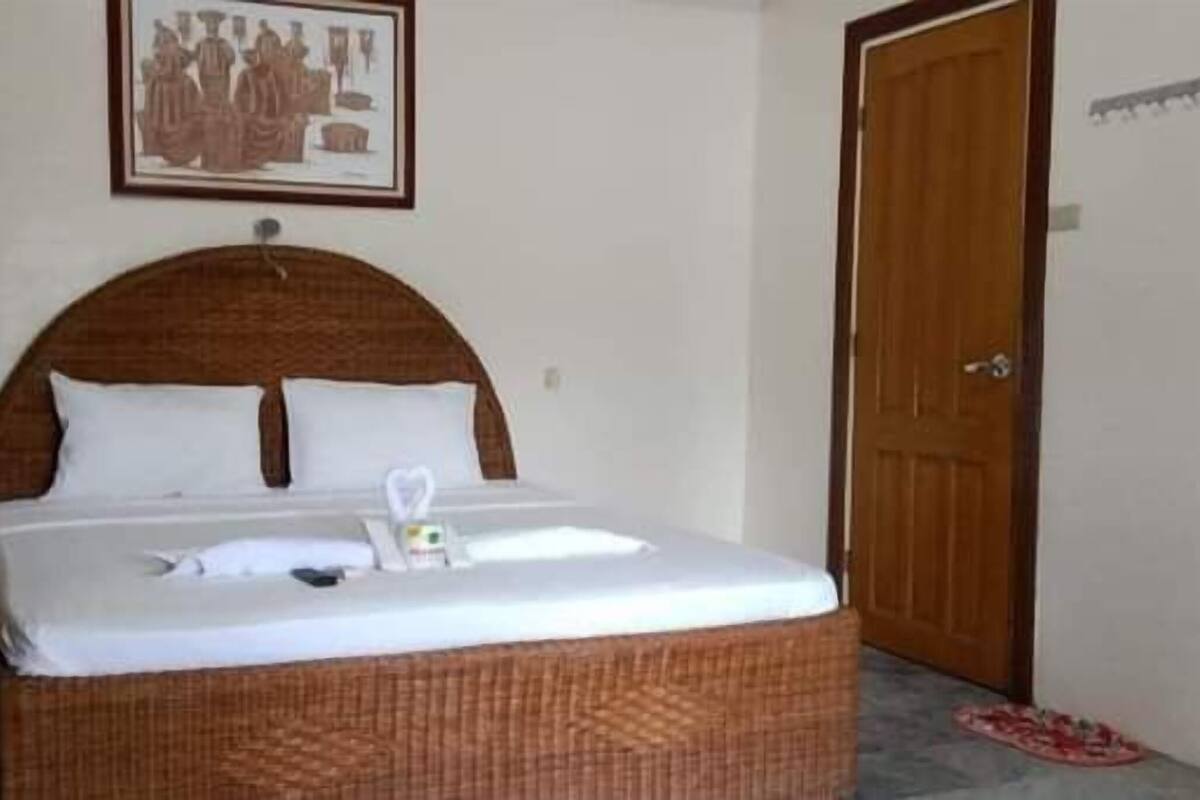 Een netjes opgemaakt bed met witte lakens, een houten hoofdbord en een ingelijst beeld erboven.