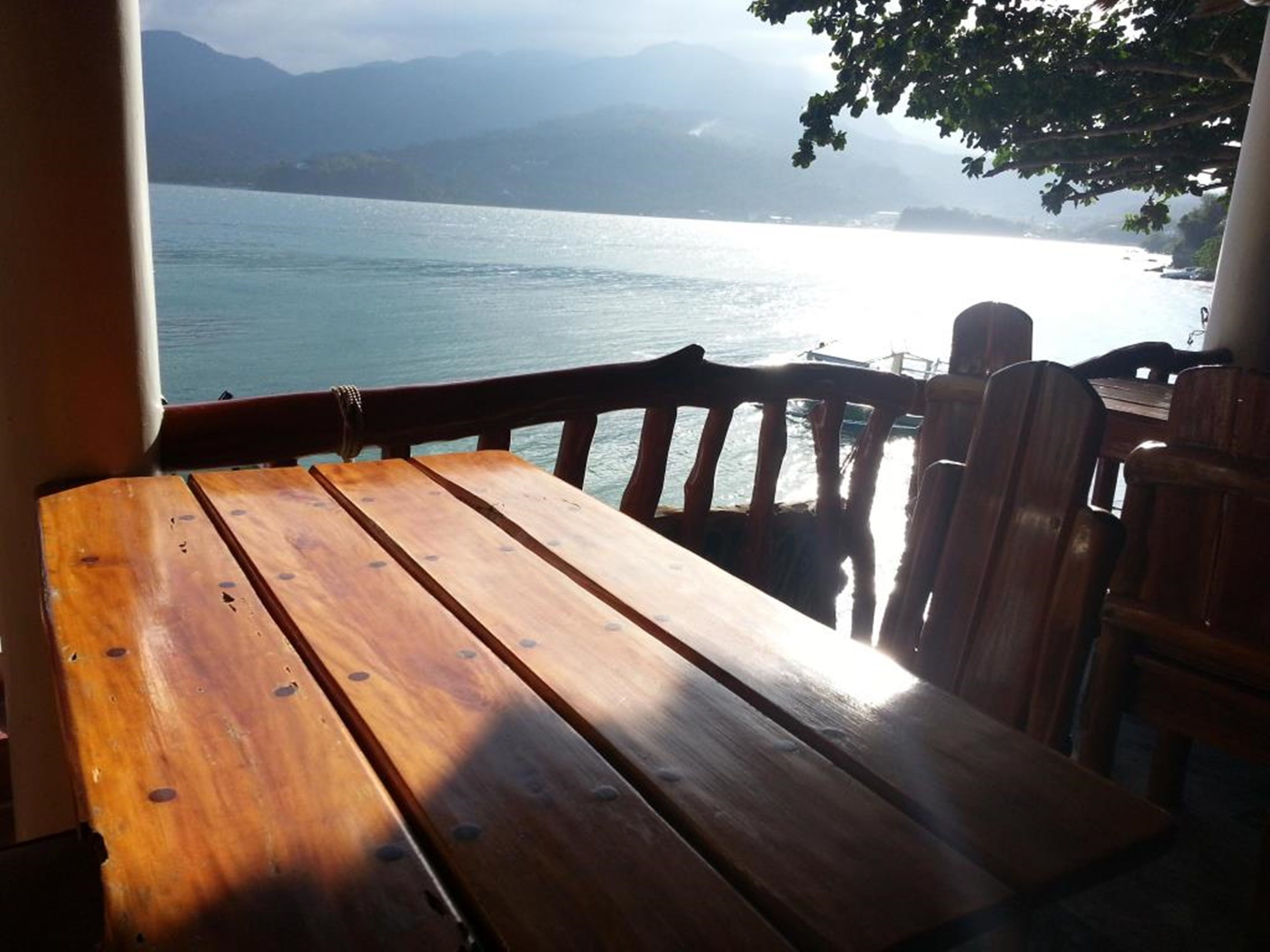 Une table en bois, dotée de pieds en métal, placée près d’une fenêtre donnant sur un plan d’eau et des montagnes lointaines.