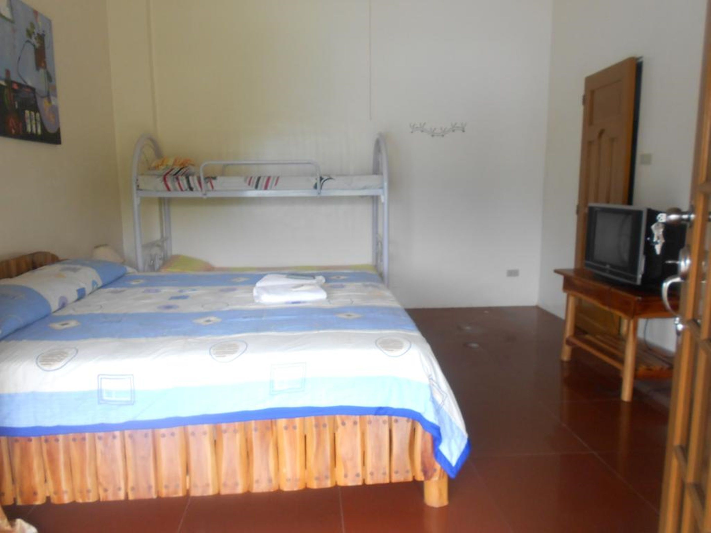 A bedroom with a bunk bed, a television on a wooden stand, and a painting on the wall.