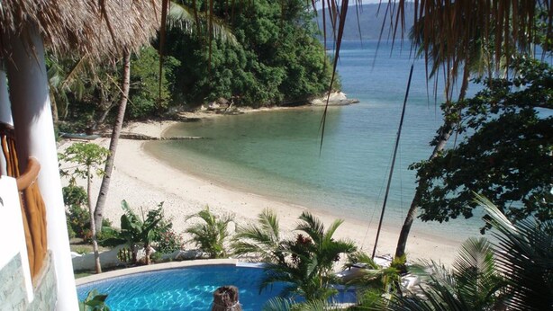 Blick auf einen Strand mit Pool und einer strohgedeckten Struktur.