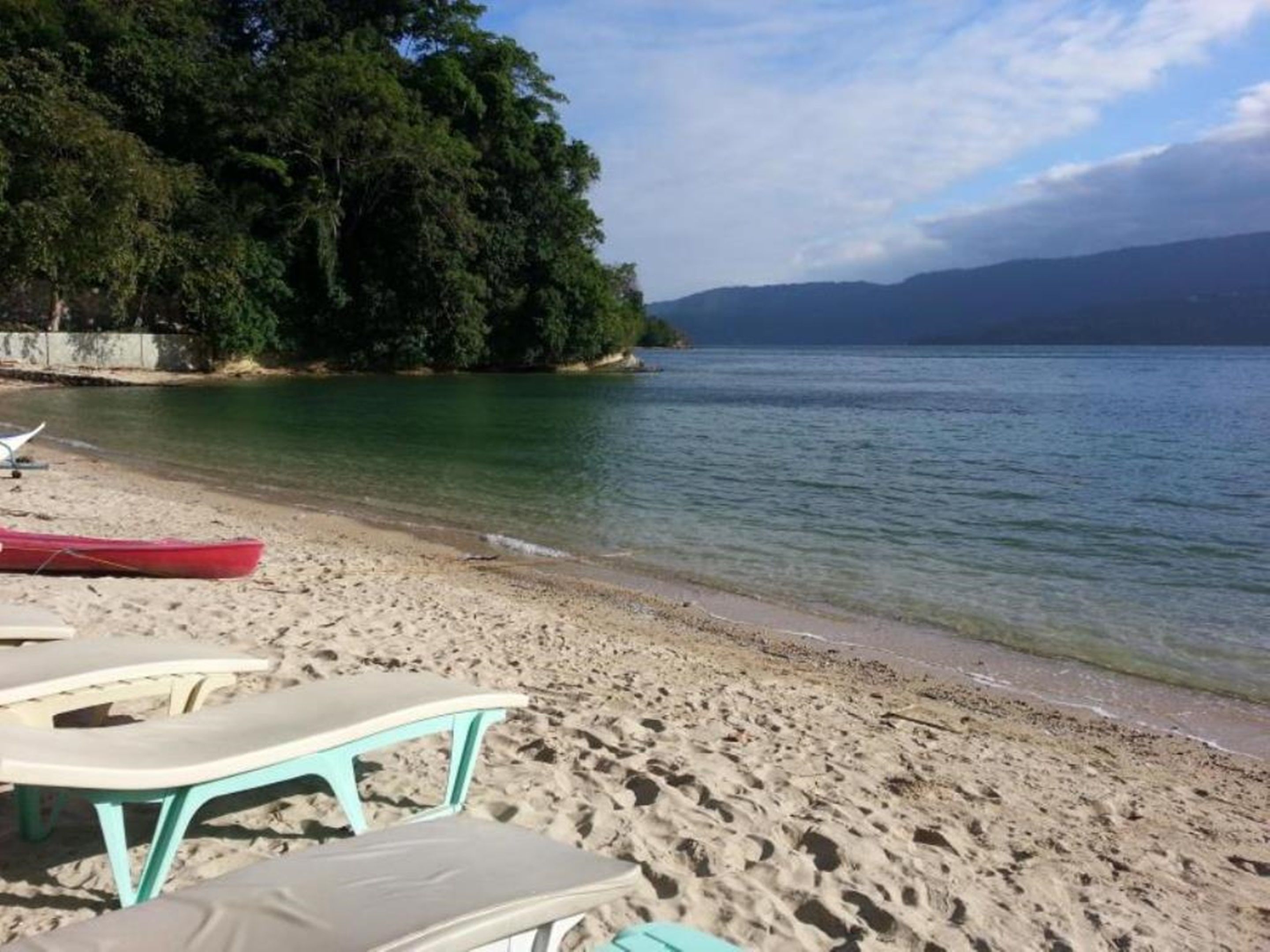 Ein Strand mit klarem Wasser, eine Reihe von Liegestühlen und ein rotes Boot.