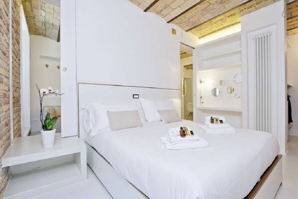 A modern hotel room with a large bed, a bedside table with a plant, and a built-in wardrobe.