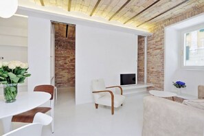 Un soggiorno moderno con un divano bianco, una poltrona bianca, un tavolino rotondo e una TV su un muro in mattoni.