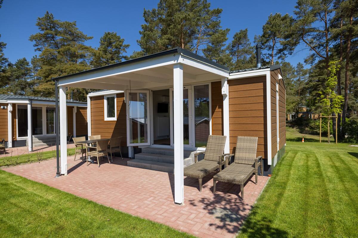 Ein modernes Haus mit überdachter Terrasse, einem Rasen und einer Holzfassade.
