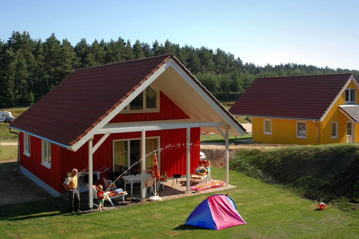 Ein rotes und gelbes Haus mit Veranda, Zelt und Rasenfläche.