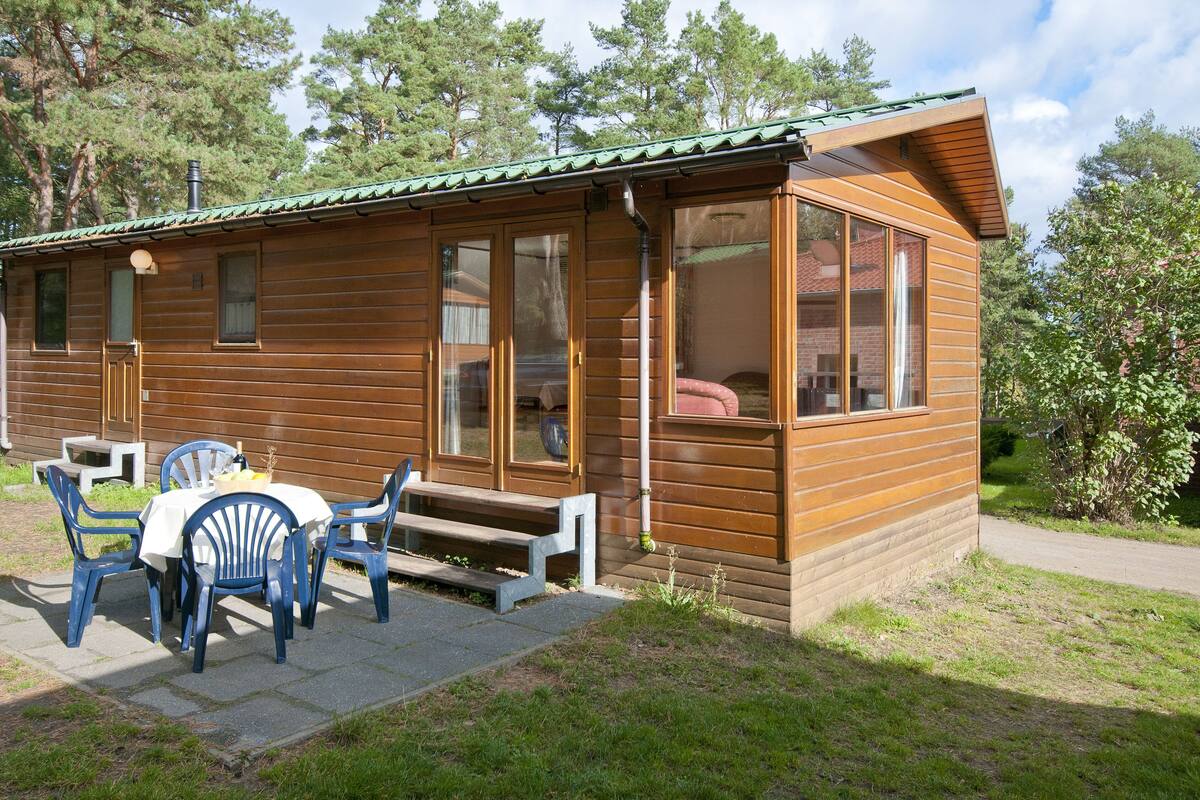 Eine Holzhütte mit Veranda, einem Tisch mit Stühlen und einem Fenster mit Blick auf die umliegenden Bäume.
