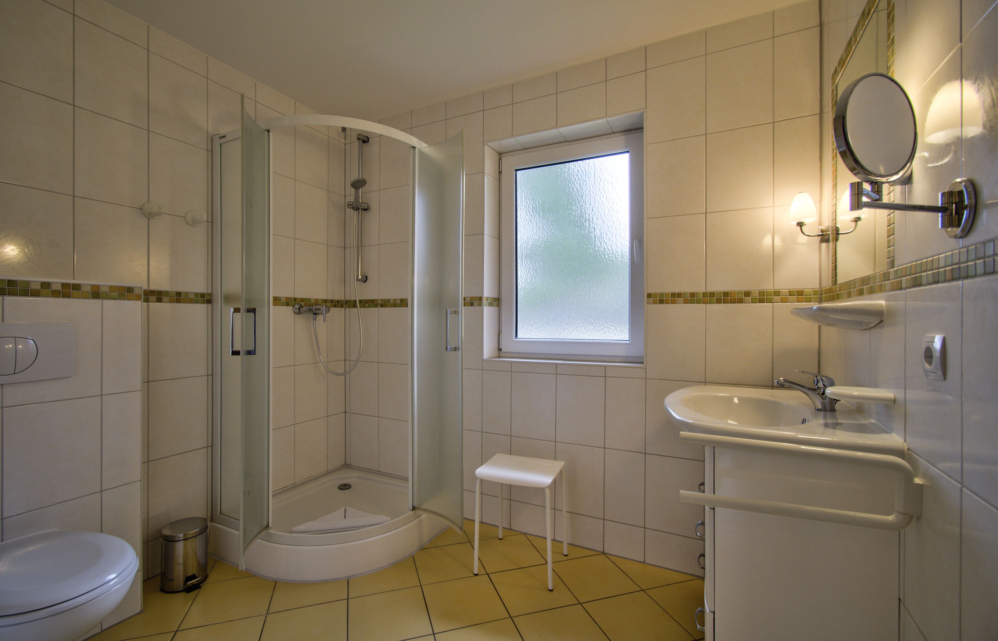 Un baño con ducha, inodoro, lavamanos y una ventana pequeña.