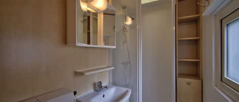 Un baño con lavamanos blanco, un espejo, ducha y ventana.