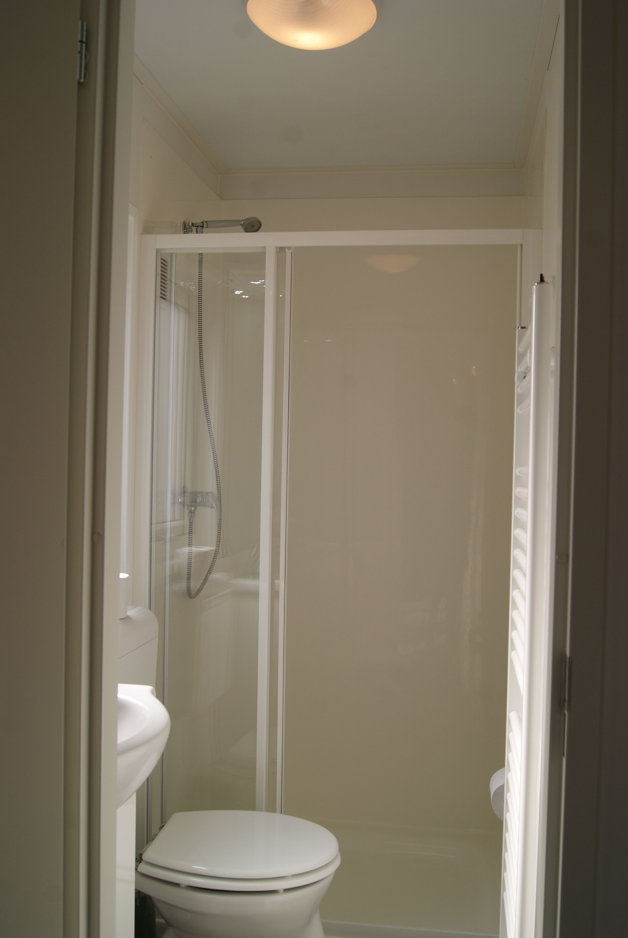 A small, enclosed bathroom with a toilet, a shower enclosure, and a glass door.