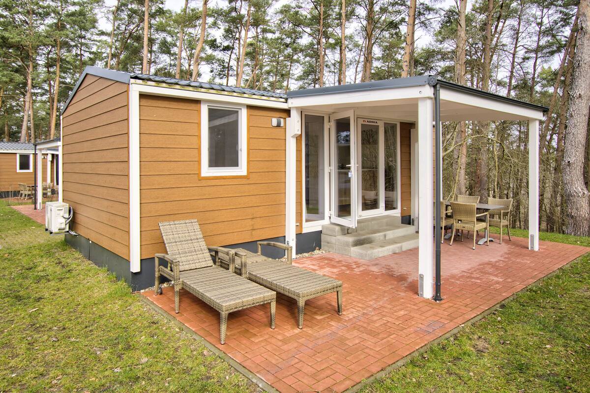 Eine kleine, eingeschossige Holzhütte mit einer Terrasse, ausgestattet mit Korbmöbeln und einem Ziegelweg.