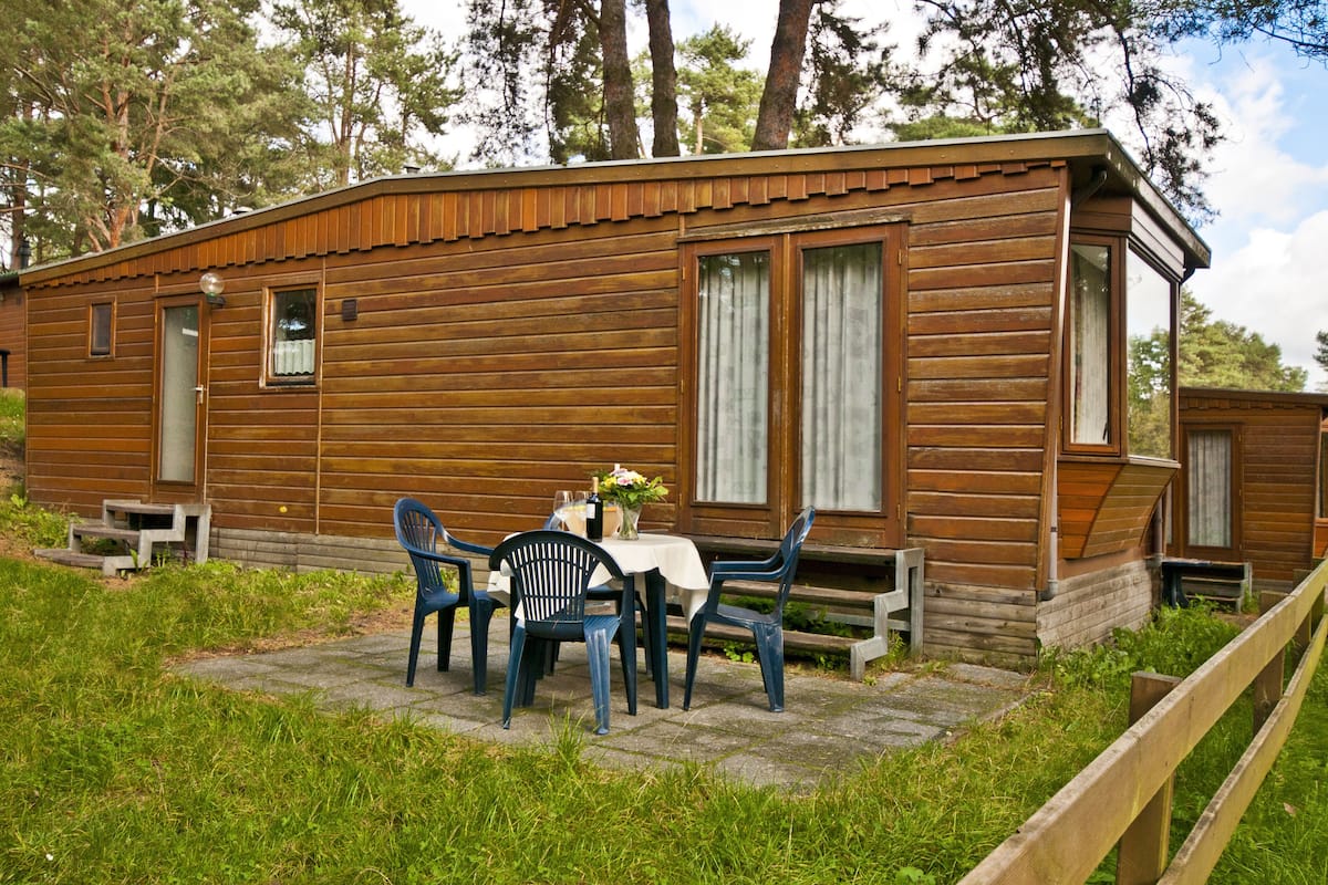 Eine Holzlaube mit einer Terrassenfläche, einem Tisch mit Stühlen und einem kleinen Garten.