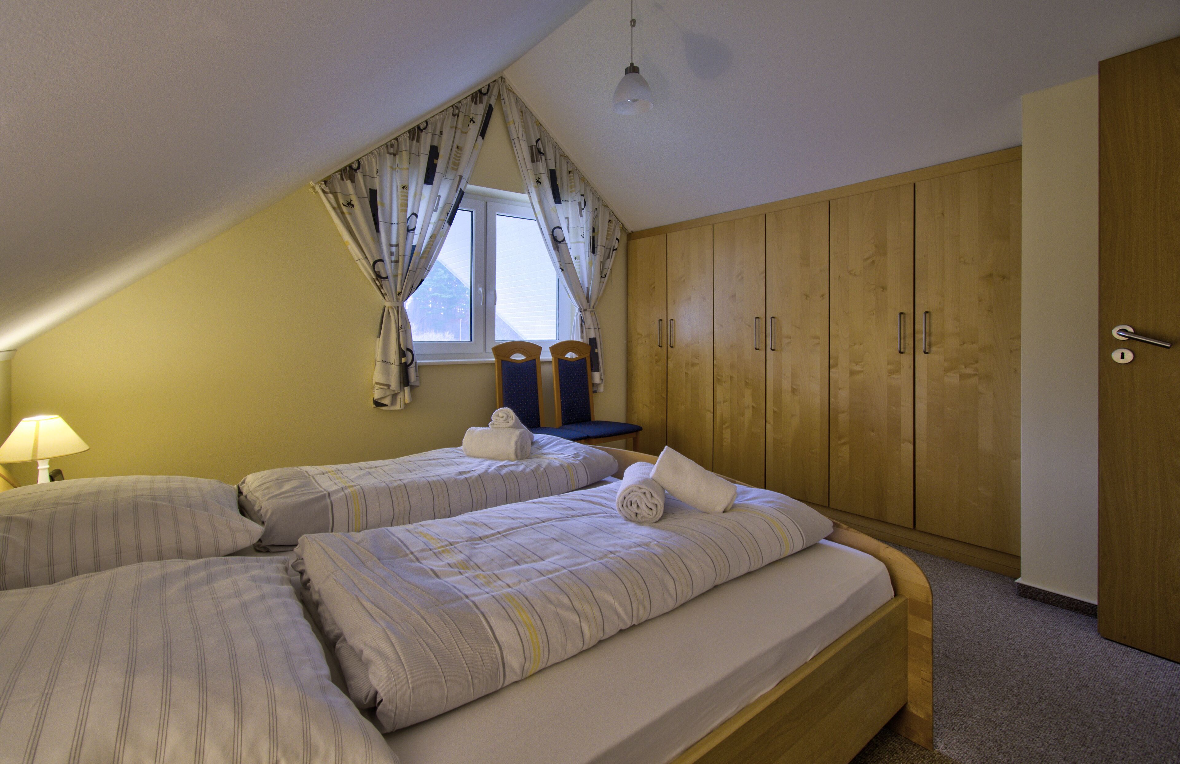 Une chambre avec deux lits, une fenêtre avec des rideaux, une armoire en bois et un bureau avec une chaise.