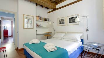 A bedroom with a bed, a desk, a chair, a bookshelf, and a door leading to another room.