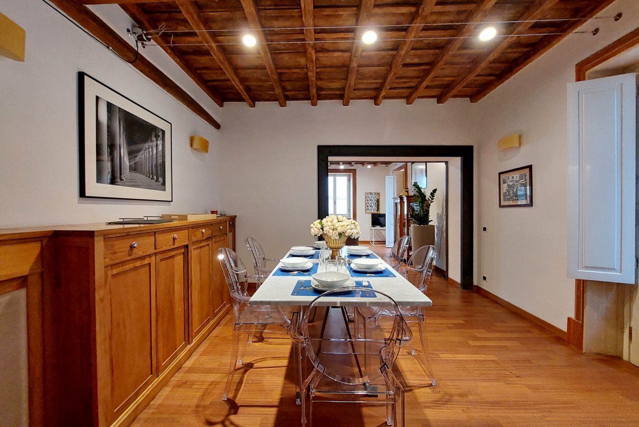 A dining area with a wooden ceiling, a long table set for six, and clear chairs.