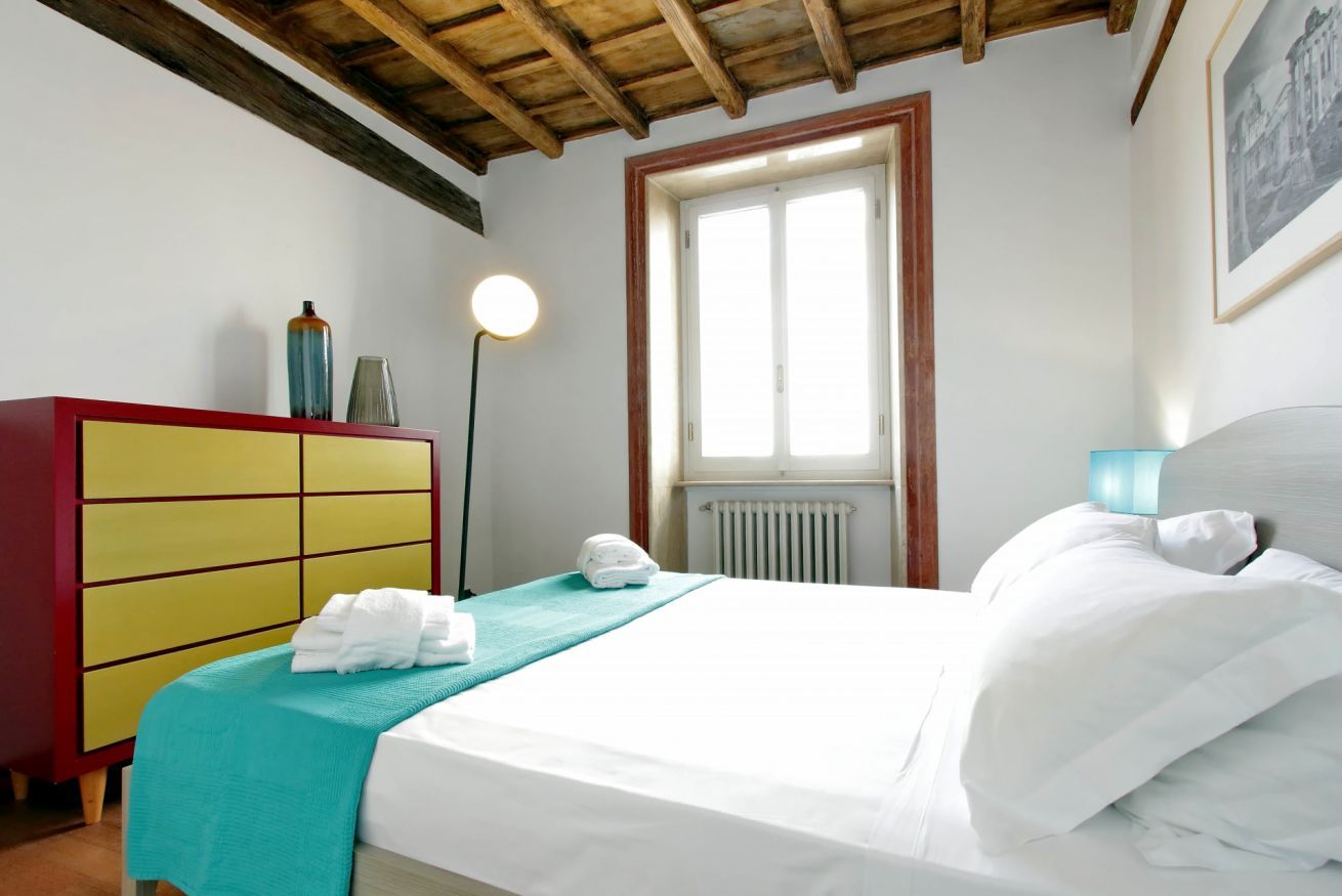 A hotel room with a bed, a red and yellow dresser, a window, and a radiator.