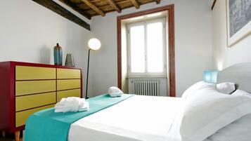 A hotel room with a bed, a red and yellow dresser, a window, and a radiator.