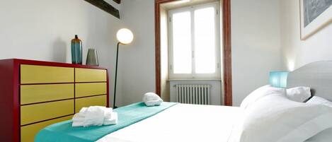 Habitación de hotel con cama, cómoda roja y amarilla, ventana y radiador.