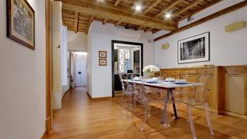 A dining area with a wooden ceiling, a long table with clear chairs, and framed pictures on the walls.