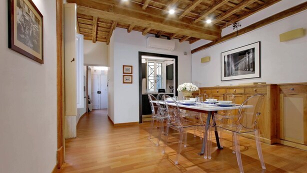 Zona pranzo con soffitto in legno, un tavolo lungo con sedie trasparenti e quadri appesi alle pareti.