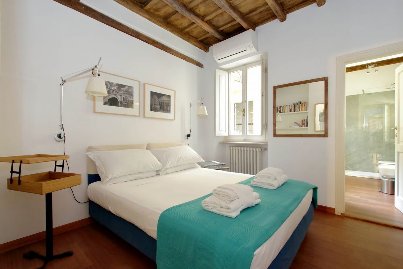A bedroom with a bed, a desk, a radiator, and a window.