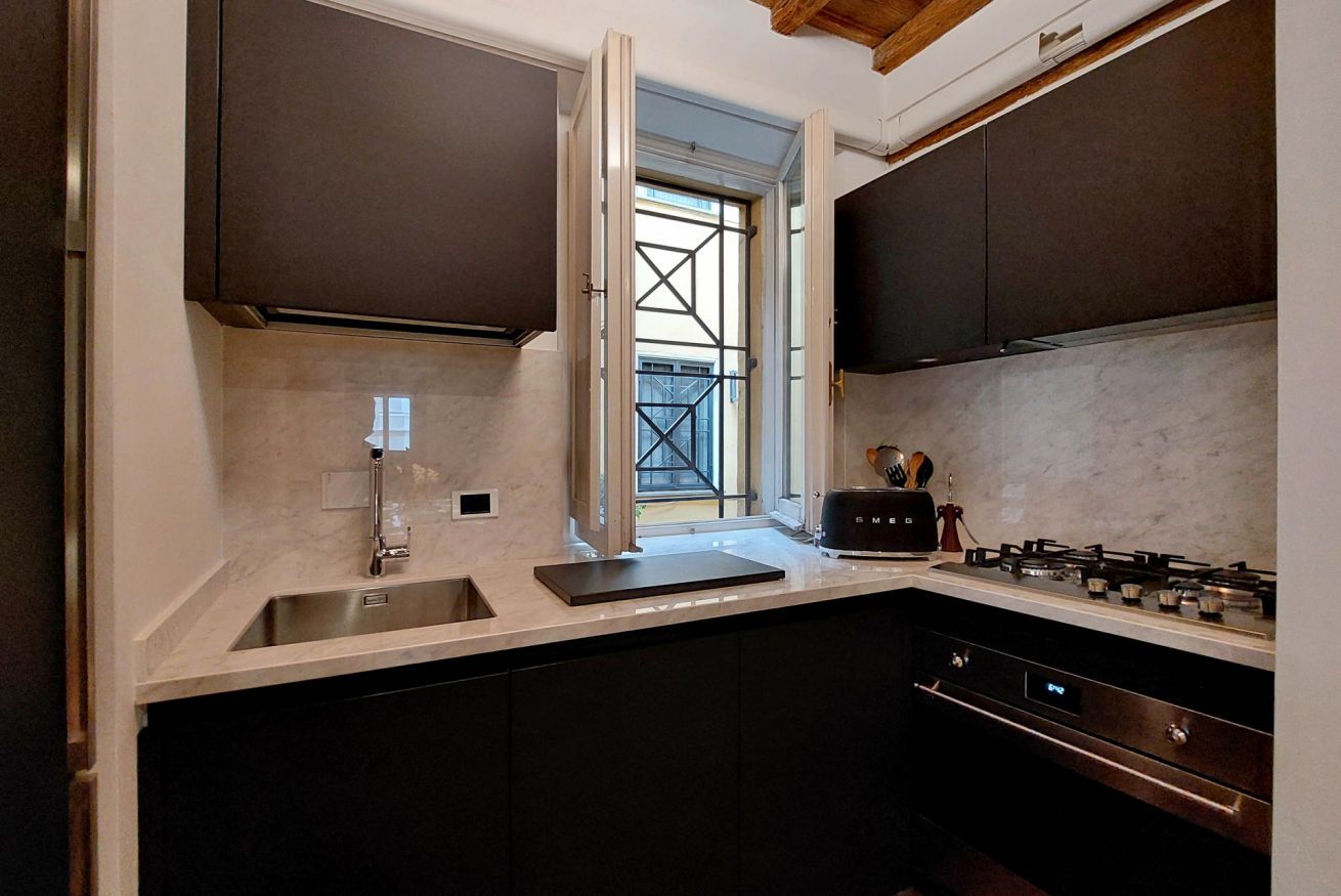 A modern kitchen with dark cabinetry, a stainless steel sink, a gas stove, and a window with a view of the outside.