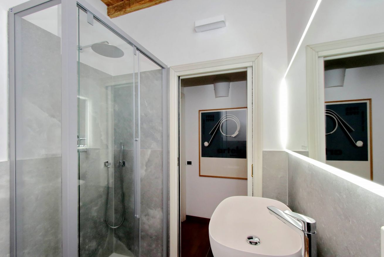 A modern bathroom with a glass shower enclosure, a white sink, and a framed picture on the wall.