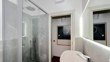 A modern bathroom with a glass shower enclosure, a white sink, and a framed picture on the wall.