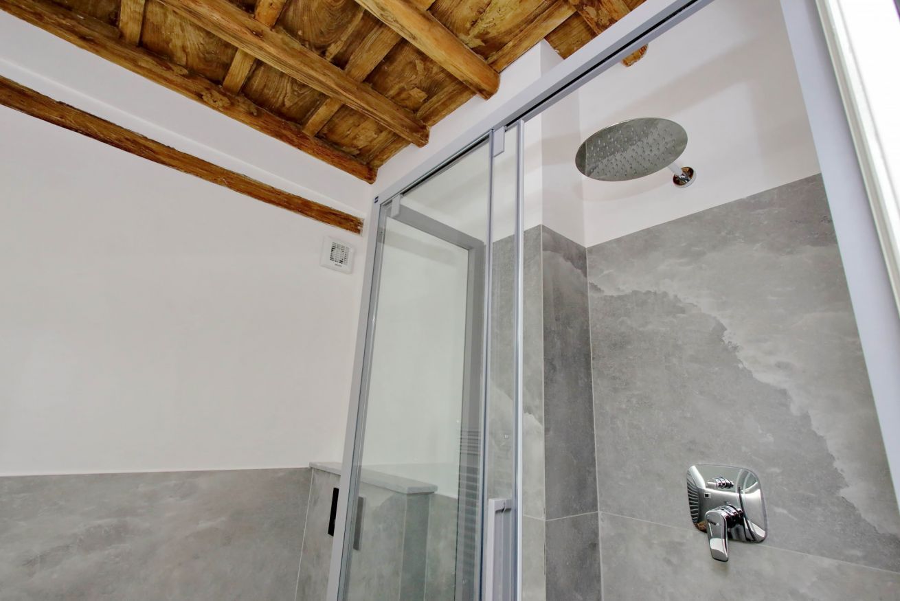 A modern bathroom with a glass shower enclosure, grey tiles, and a wooden ceiling.
