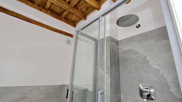A modern bathroom with a glass shower enclosure, grey tiles, and a wooden ceiling.