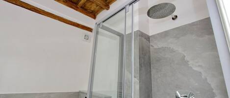 A modern bathroom with a glass shower enclosure, grey tiles, and a wooden ceiling.