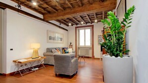Un soggiorno con soffitto in legno, un divano grigio, un tavolino con una lampada e una grande pianta in vaso.