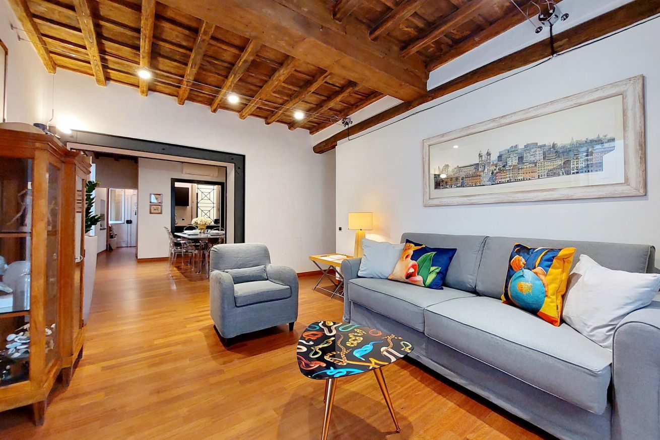 A living room with a wooden ceiling, a sofa with colorful cushions, a side table, and a framed cityscape picture on the wall.