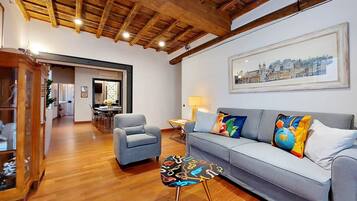 A living room with a wooden ceiling, a sofa with colorful cushions, a side table, and a framed cityscape picture on the wall.