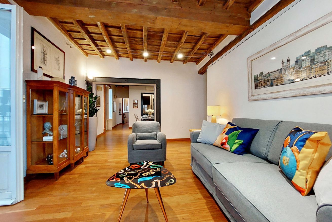 A living room with a grey sofa, colorful cushions, a wooden cabinet, and a small round table.