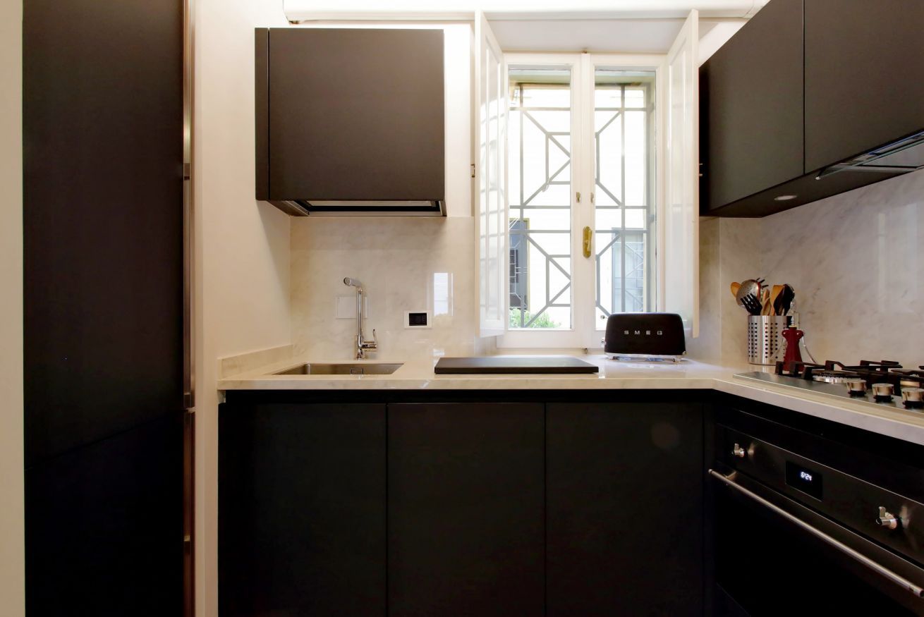 A modern kitchen with dark cabinetry, a built-in oven, and a window providing natural light.